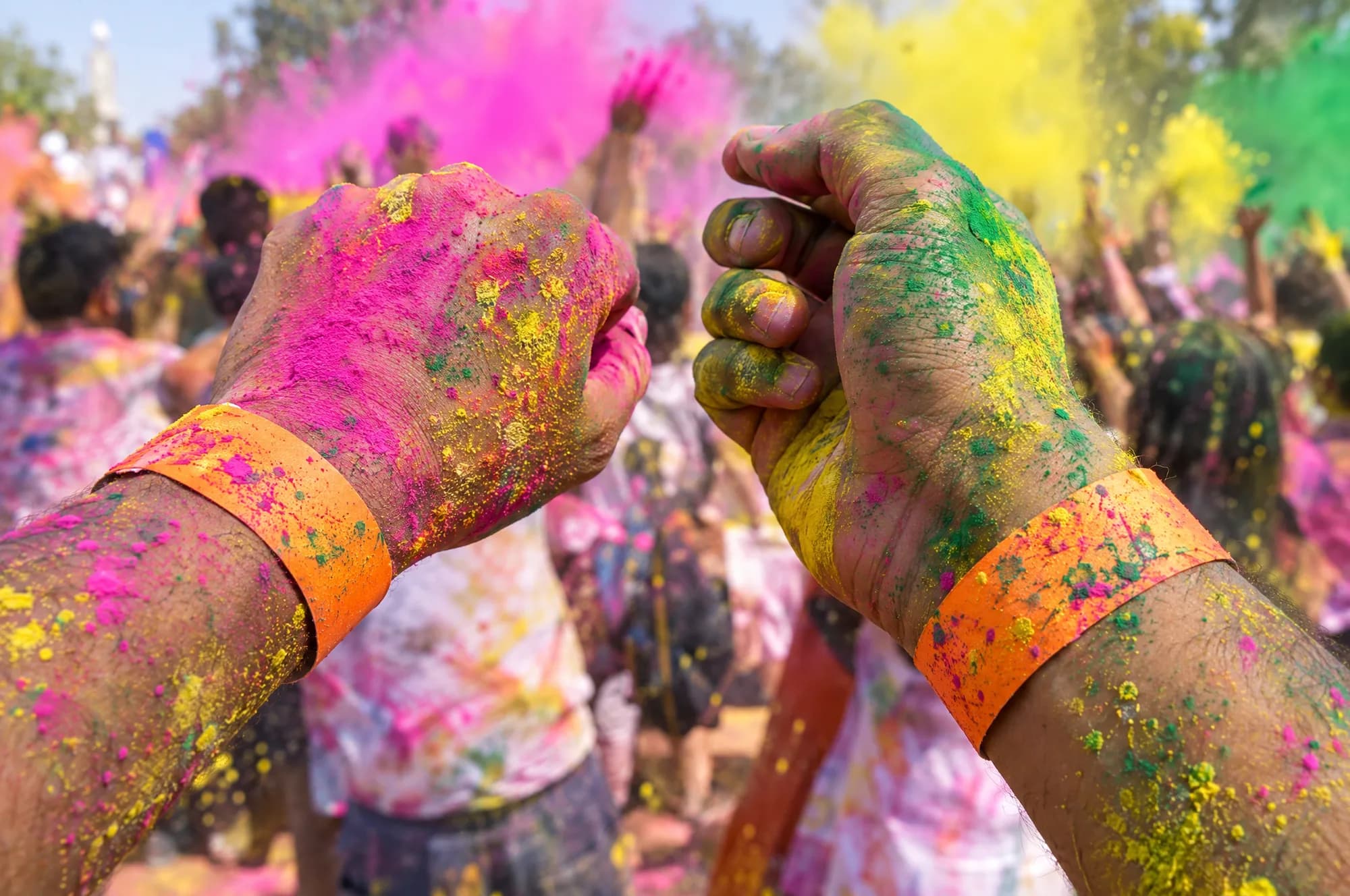 Hands covered in pink, yellow and green colour, each wearing an orange paper wristband