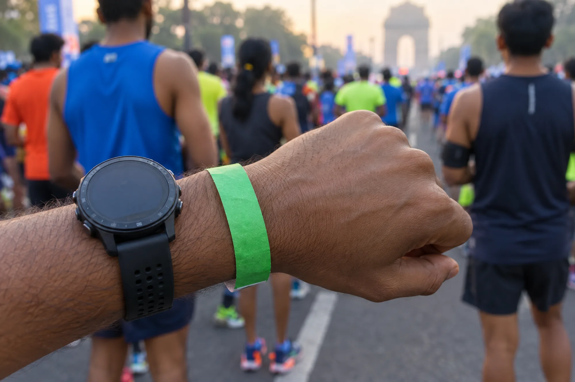 A runner’s wrist with a green paper wristband and a sports watch at a race start