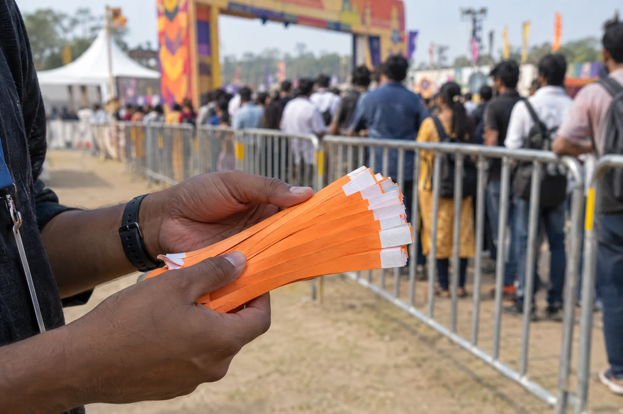 An organiser holding a thick bundle of orange paper wristbands at a festival entry gate