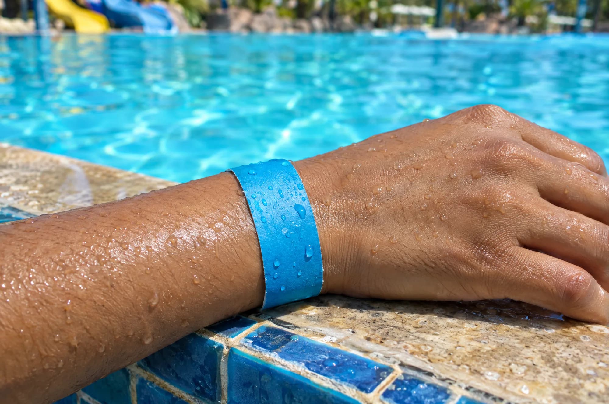 A wet wrist wearing a blue paper wristband on the edge of a pool